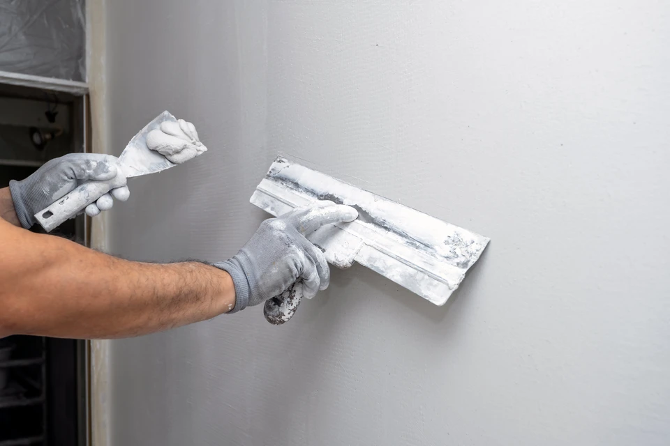 Un artisan applique de l'enduit de lissage sur un mur intérieur blanc à l'aide d'une spatule large