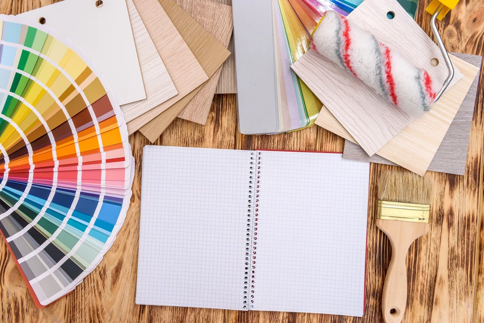 Espace de travail d'architecte d'intérieur avec nuancier de couleurs étalé, échantillons de bois et matériaux, carnet à spirale ouvert, pinceau et rouleau de peinture sur table en bois brut