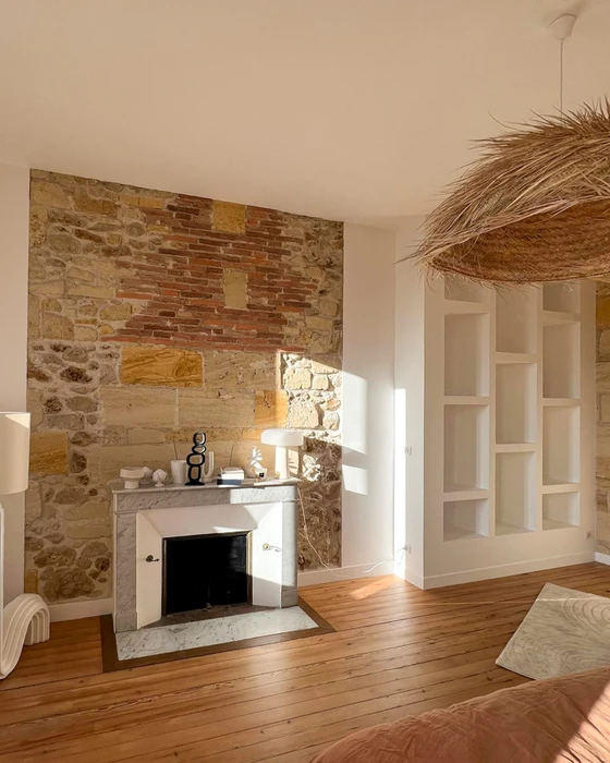 Salon avec cheminée en marbre blanc sur mur en pierres apparentes mêlant moellons et briques