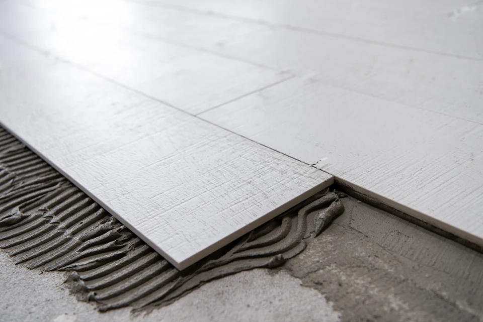 Chantier de pose de carrelage en cours, sol intérieur avec carreaux blancs rectangulaires partiellement installés
