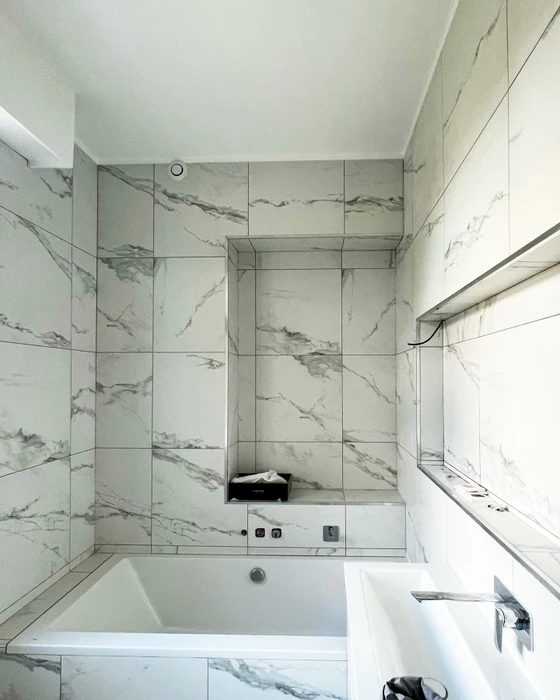 Salle de bain luxueuse vue en plongée, baignoire encastrée blanche, parois en grands carreaux effet marbre blanc veiné gris type Statuario