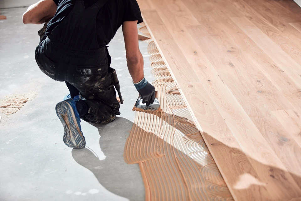 Homme en tenue de travail installant du parquet dans une pièce en rénovation, agenouillé sur le sol, utilisant un marteau pour ajuster les lames de bois