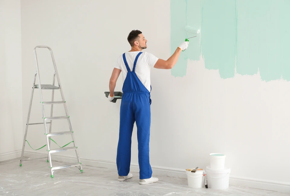 Peintre professionnel appliquant de la peinture murale blanche avec un rouleau dans un espace intérieur